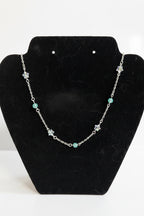 A silver-toned beaded necklace with star and round bead accents, displayed on a black velvet jewelry bust against a white background.