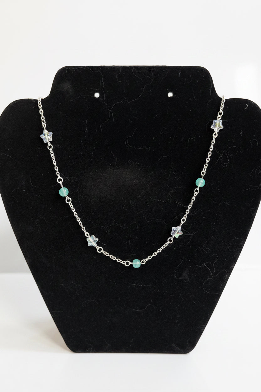 A silver-toned beaded necklace with star and round bead accents, displayed on a black velvet jewelry bust against a white background.