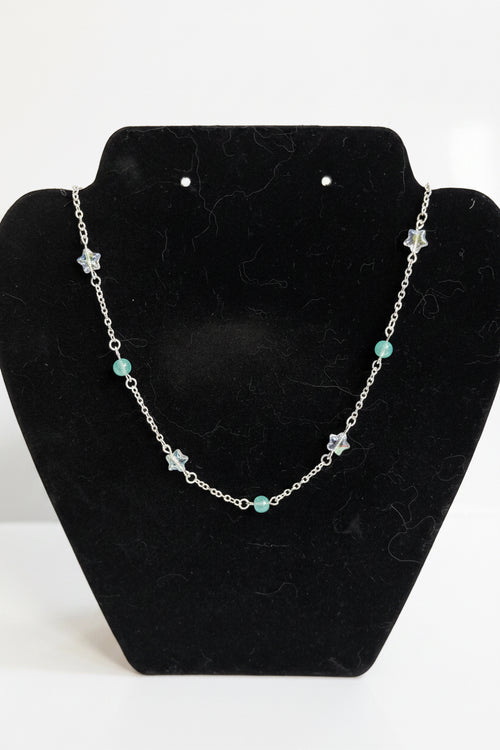 A silver-toned beaded necklace with star and round bead accents, displayed on a black velvet jewelry bust against a white background.