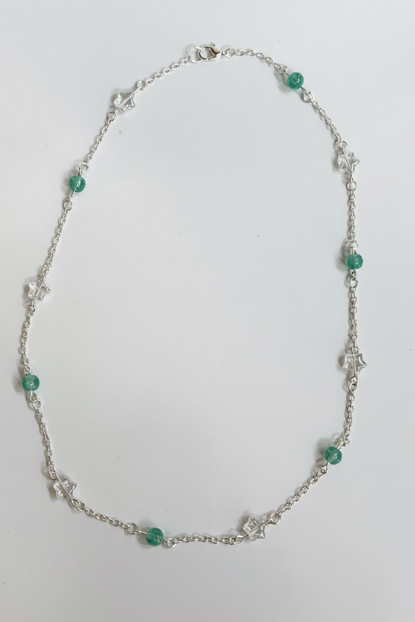 A delicate silver chain necklace featuring small green faceted beads and silver star-shaped charms, displayed on a plain light gray surface.