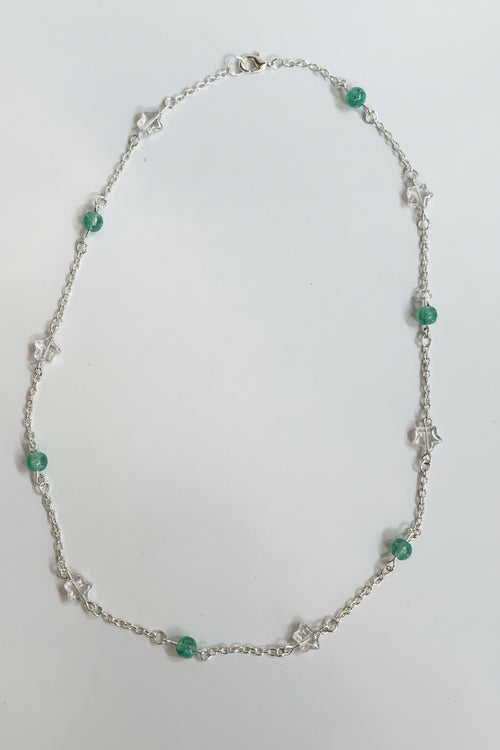 A delicate silver chain necklace featuring small green faceted beads and silver star-shaped charms, displayed on a plain light gray surface.