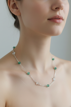 A close-up of a woman wearing a delicate silver chain necklace with small green beads and white flower-shaped accents.