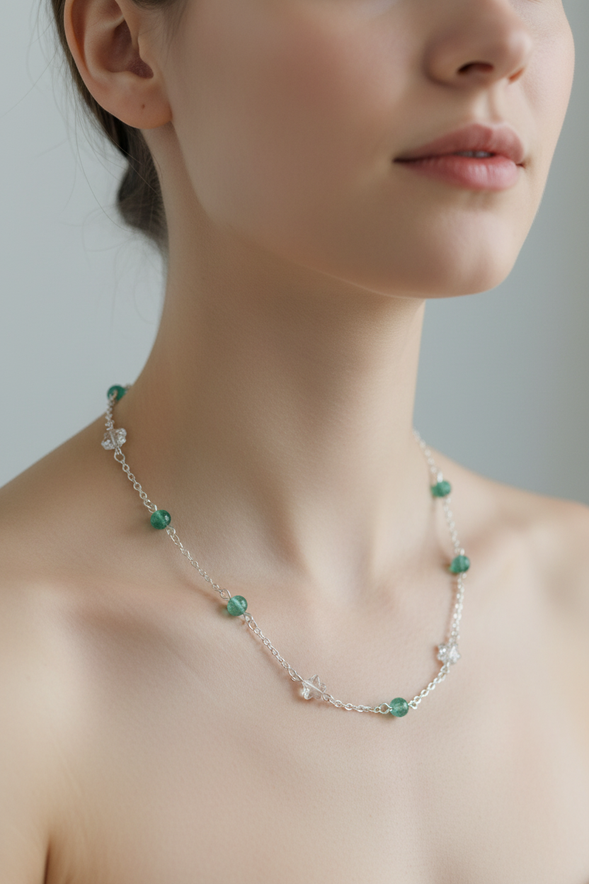 A close-up of a woman wearing a delicate silver chain necklace with small green beads and white flower-shaped accents.