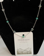 A silver-toned beaded necklace with small turquoise-green beads and star-shaped charms, displayed on a black velvet jewelry stand with a white hangtag.