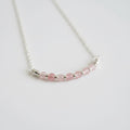 Necklace with pink beads and silver accents on a light gray background