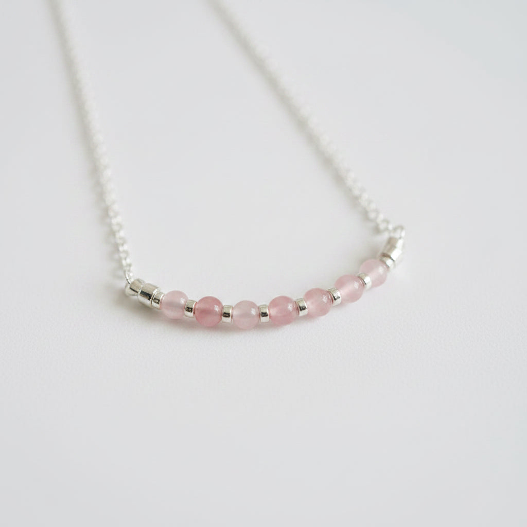 Necklace with pink beads and silver accents on a light gray background