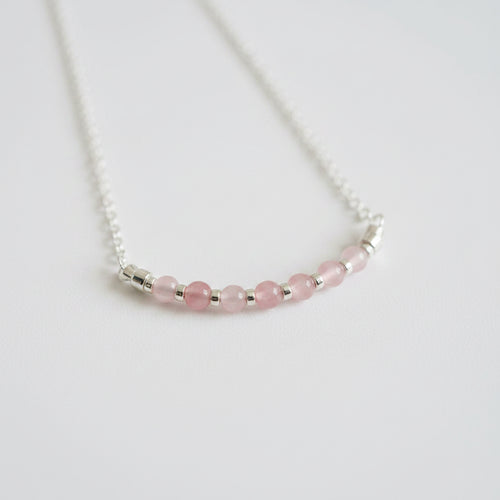 Necklace with pink beads and silver accents on a light gray background