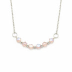 A silver chain necklace featuring a curved row of faceted iridescent beads in soft pink and white, separated by small silver spacer beads, with two silver O-ring connectors, shown on a plain white background.