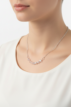 A delicate silver chain necklace featuring a curved bar of small, faceted iridescent beads in pale pink and white, displayed on a clean white background.