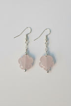 A pair of dangle earrings featuring light pink rose quartz flower-shaped beads suspended from silver fishhook wires, shown on a plain light gray background.