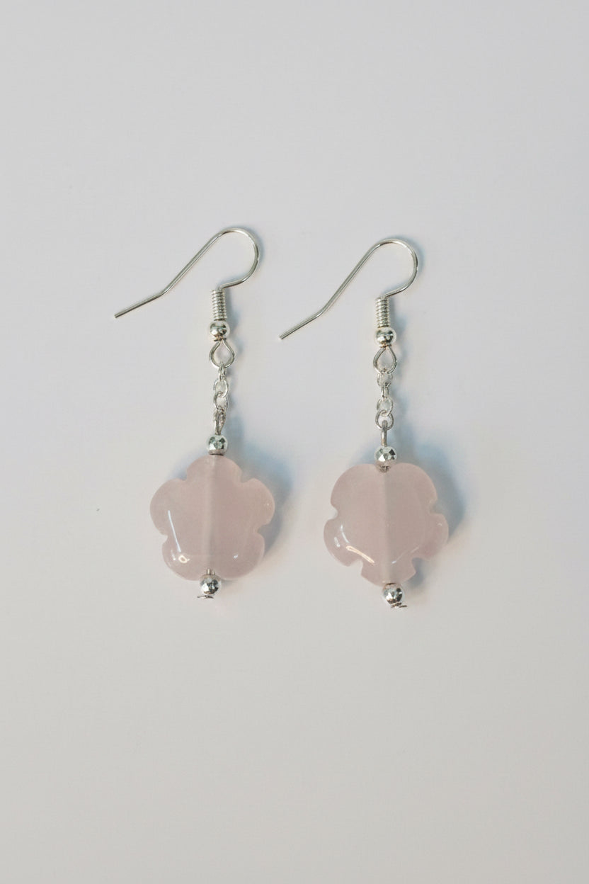 A pair of dangle earrings featuring light pink rose quartz flower-shaped beads suspended from silver fishhook wires, shown on a plain light gray background.