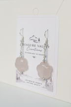 A pair of rose quartz flower-shaped drop earrings with silver hooks, displayed on a white backing card from Treasure Valley Creations.