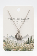 Treasure Valley Creations silver crescent moon necklace with a tree design, displayed on a cream-colored backing card featuring a mountain and wildflower illustration.
