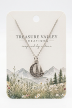 Treasure Valley Creations silver crescent moon necklace with a tree design, displayed on a cream-colored backing card featuring a mountain and wildflower illustration.