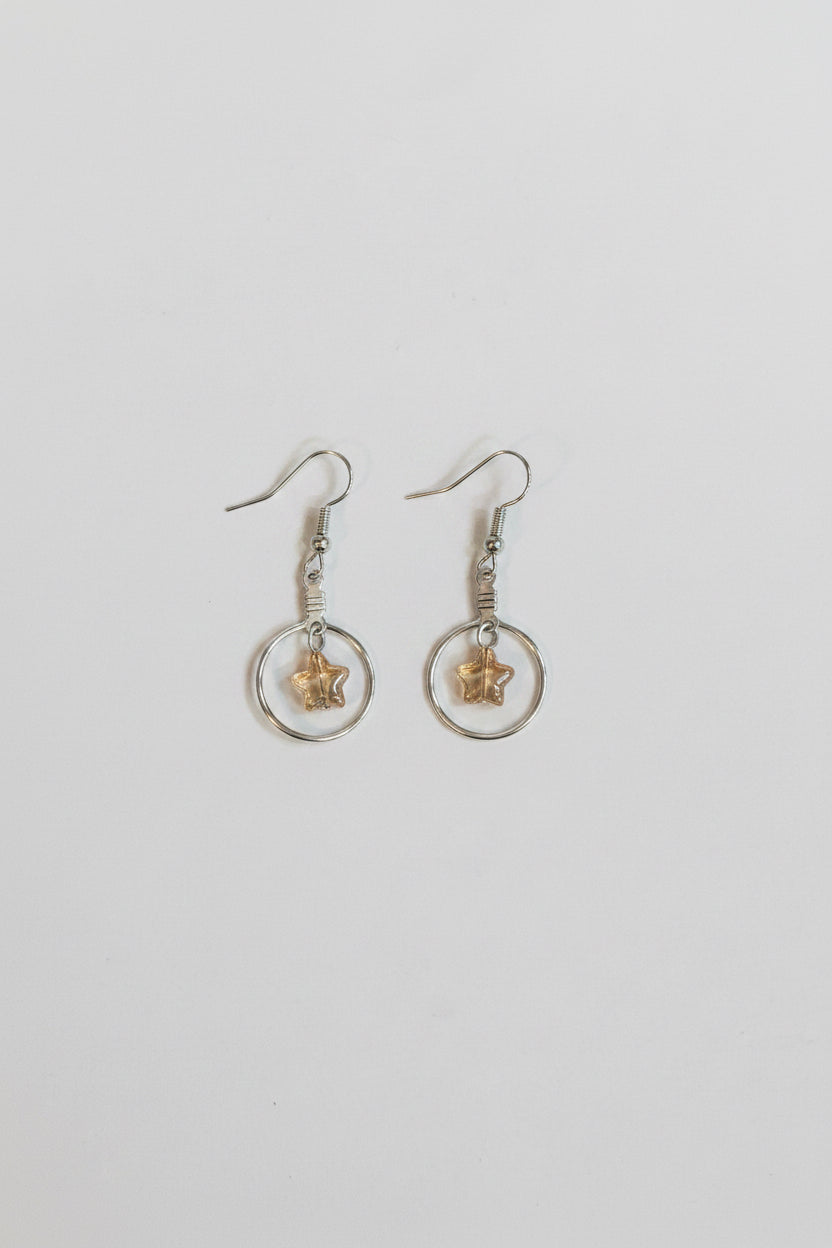 A pair of silver-toned dangle earrings with circular wire hoops, small clear stones, and a central gold-toned star-shaped charm, displayed on a plain light gray background.