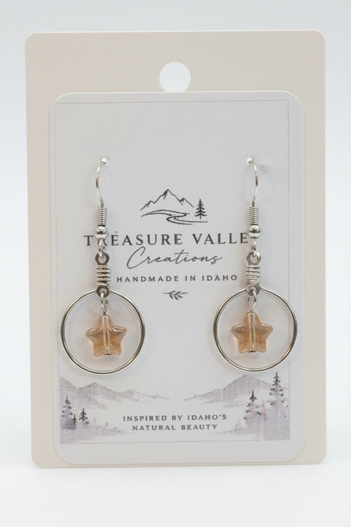 Treasure Valley Creations handmade dangle earrings with silver-toned circular hoops, wrapped wire, and star-shaped amber pendants, displayed on a branded white backing card.
