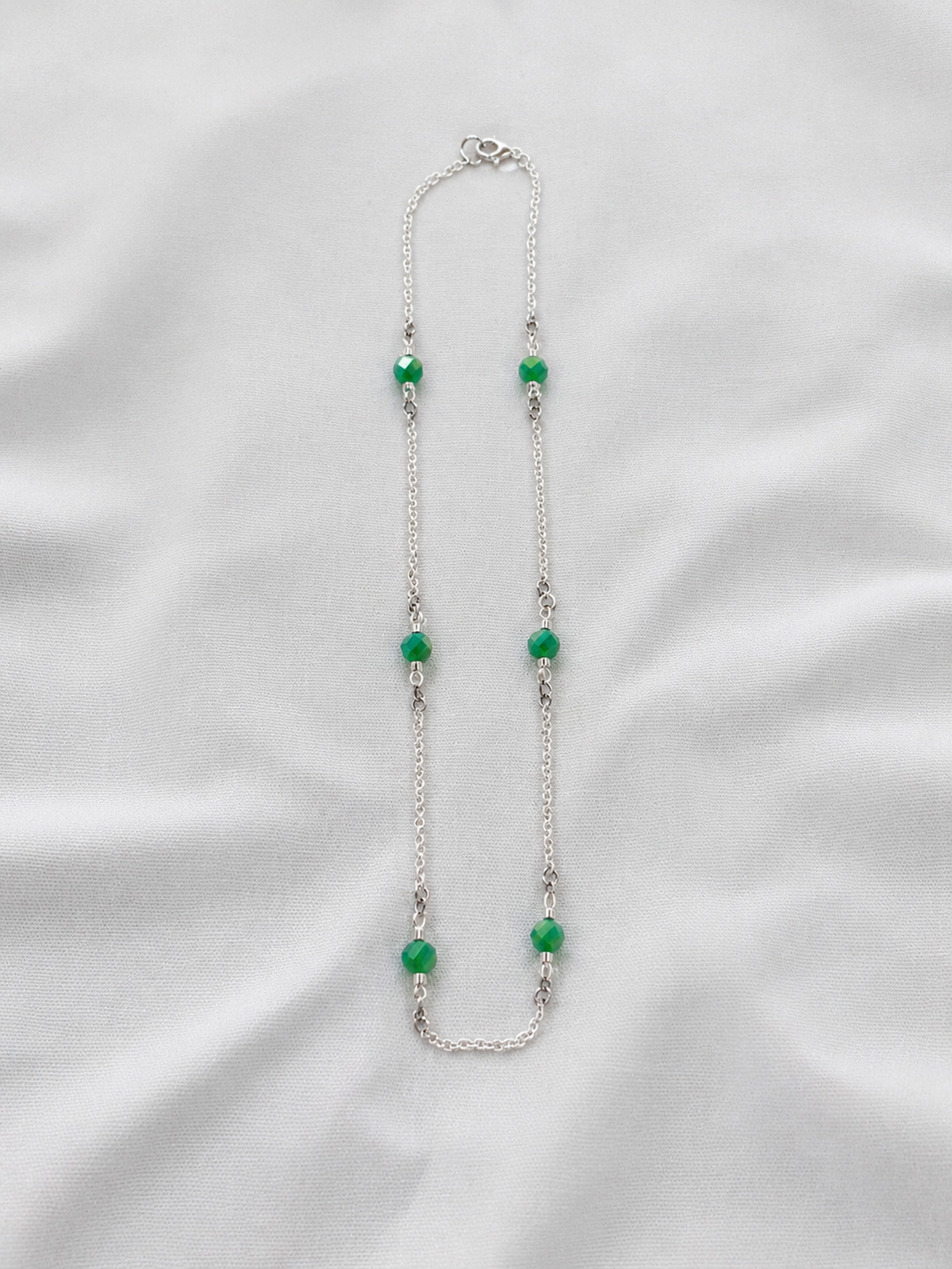 Necklace with green beads on a white fabric background