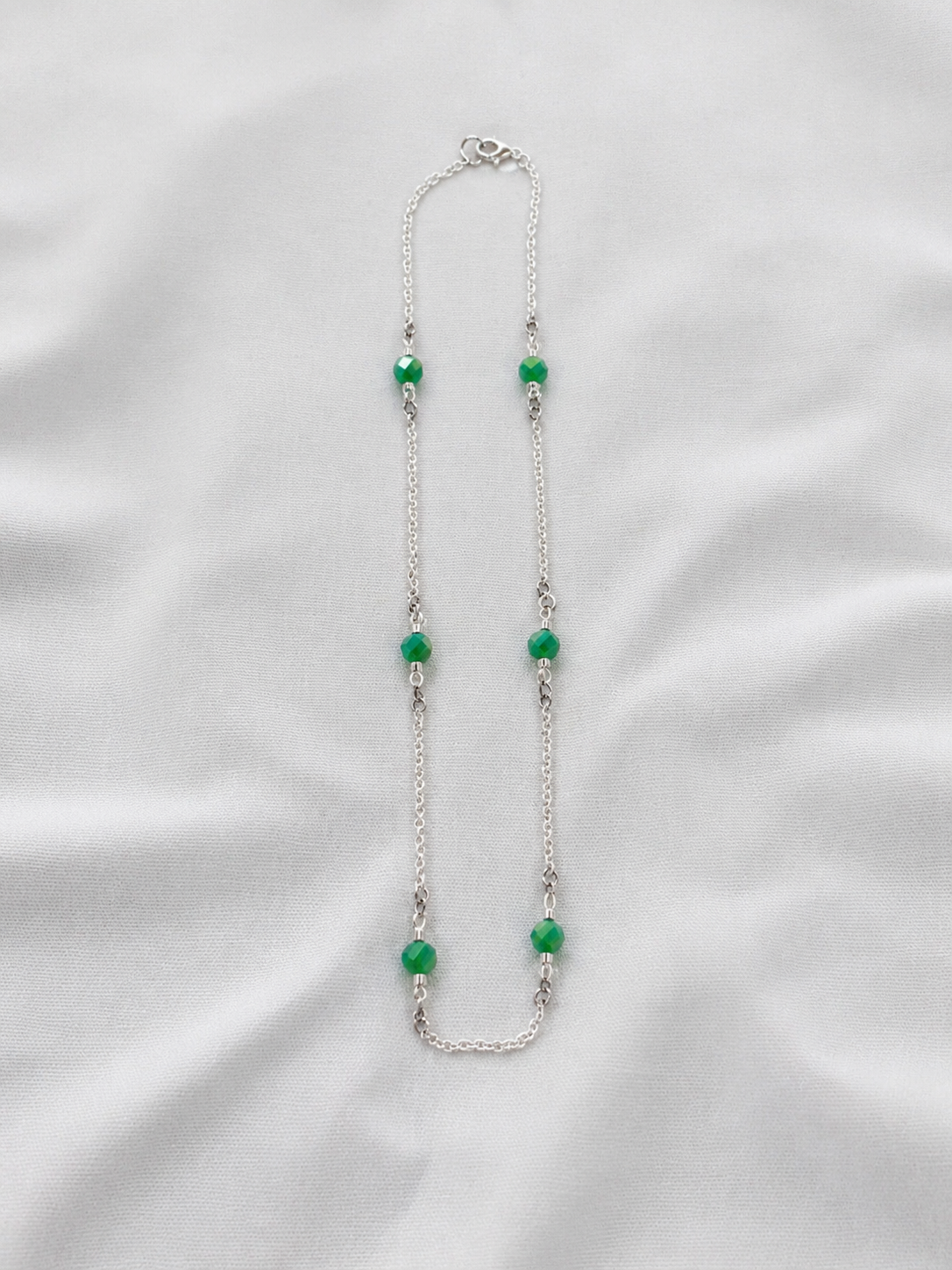 Necklace with green beads on a white fabric background