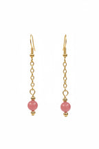 Gold dangle earrings with a small pink bead at the bottom, displayed against a black background.