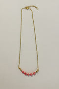 A delicate gold chain necklace featuring a row of small, round pink beads at the center, displayed against a plain off-white background.