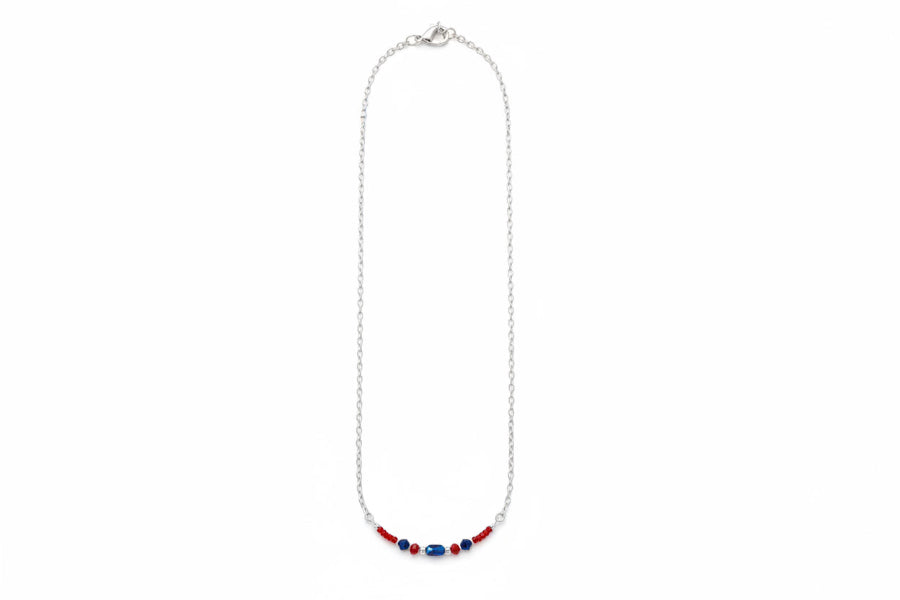 A delicate silver chain necklace featuring a short section at the bottom adorned with small red and blue beads, shown against a plain white background.