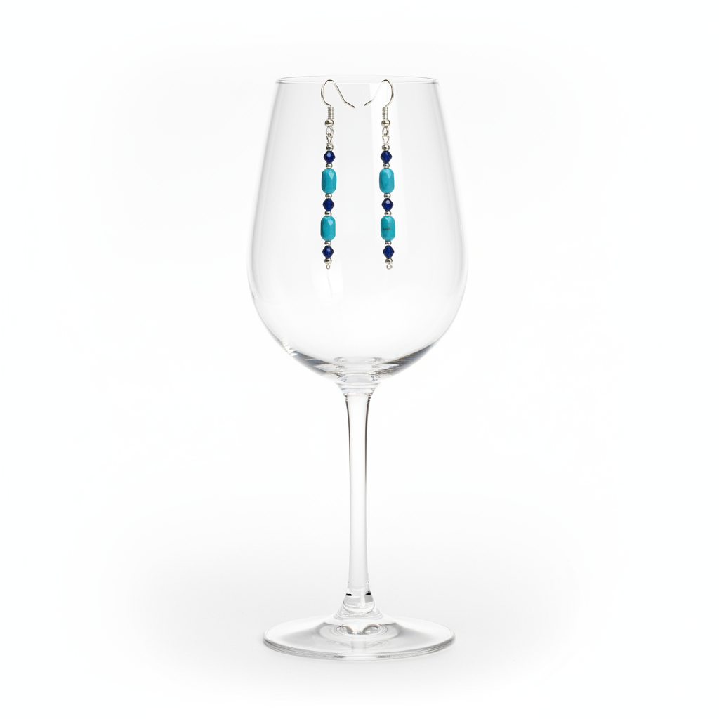A pair of silver dangle earrings with turquoise and dark blue beads, hanging from the rim of a clear wine glass on a white background.