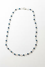 A beaded chain necklace with alternating dark blue faceted beads and silver-toned metal links, displayed on a plain light gray surface.
