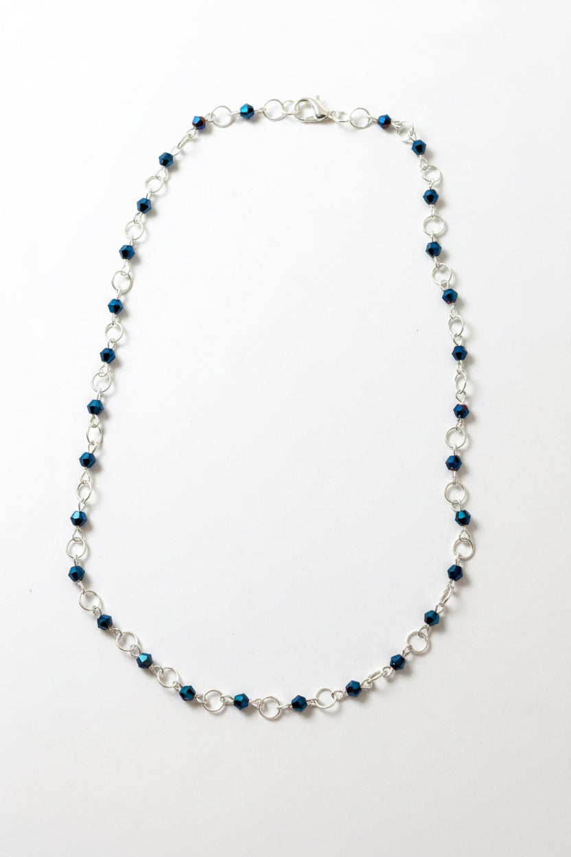 A beaded chain necklace with alternating dark blue faceted beads and silver-toned metal links, displayed on a plain light gray surface.