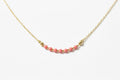 A delicate gold chain necklace featuring a central row of small pink beads separated by tiny gold spacer beads, displayed on a black background.
