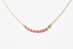 A delicate gold chain necklace featuring a central row of small pink beads separated by tiny gold spacer beads, displayed on a black background.