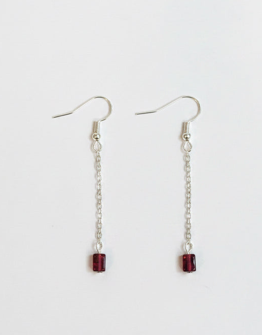 A pair of silver dangle earrings with small rectangular dark red gemstone charms, displayed on a clean white background.
