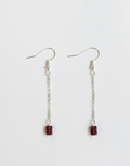 A pair of silver dangle earrings with small rectangular dark red gemstone charms, displayed on a clean white background.
