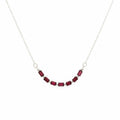A delicate silver chain necklace featuring a curved row of small rectangular dark red gemstones, displayed on a plain light gray background.