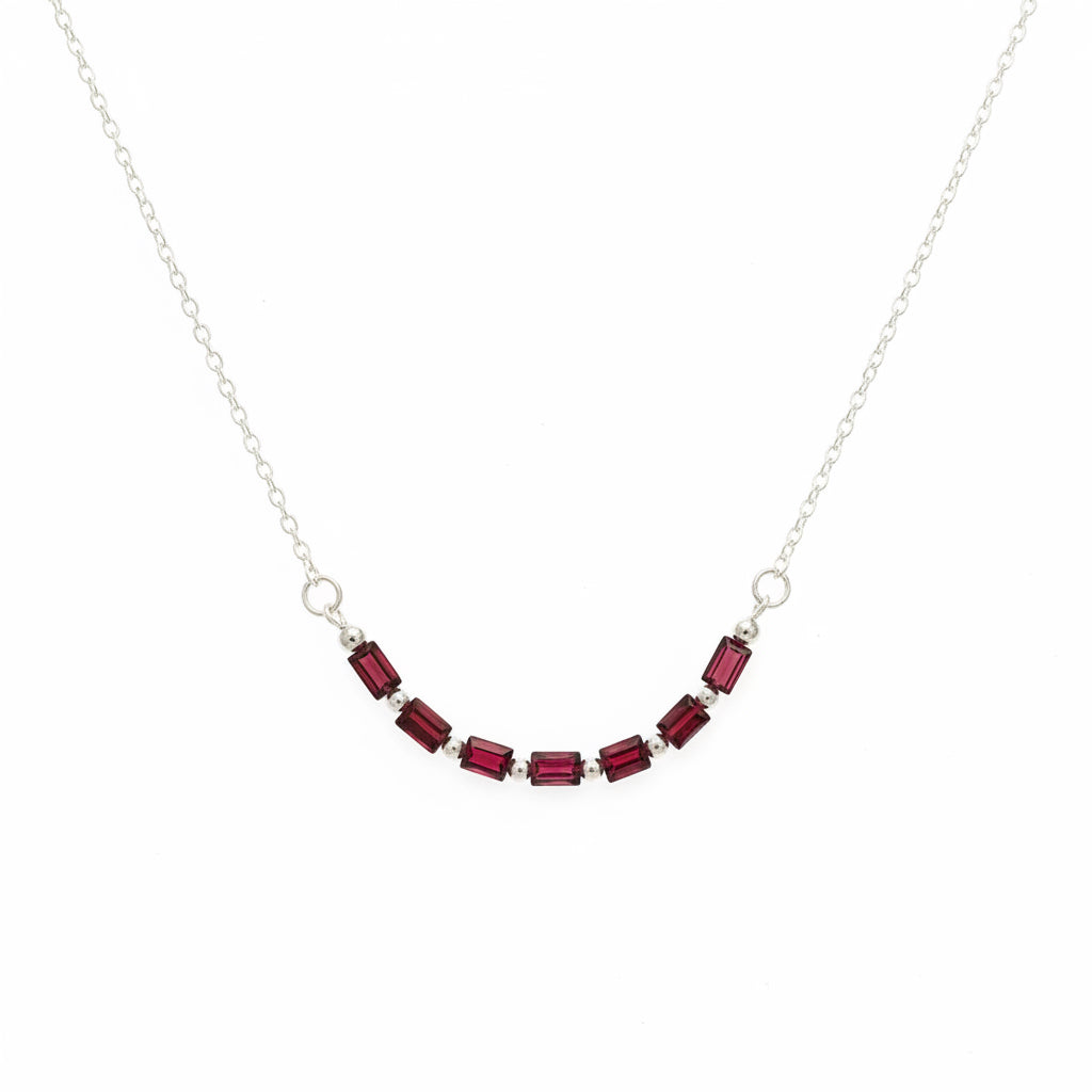 A delicate silver chain necklace featuring a curved row of small rectangular dark red gemstones, displayed on a plain light gray background.