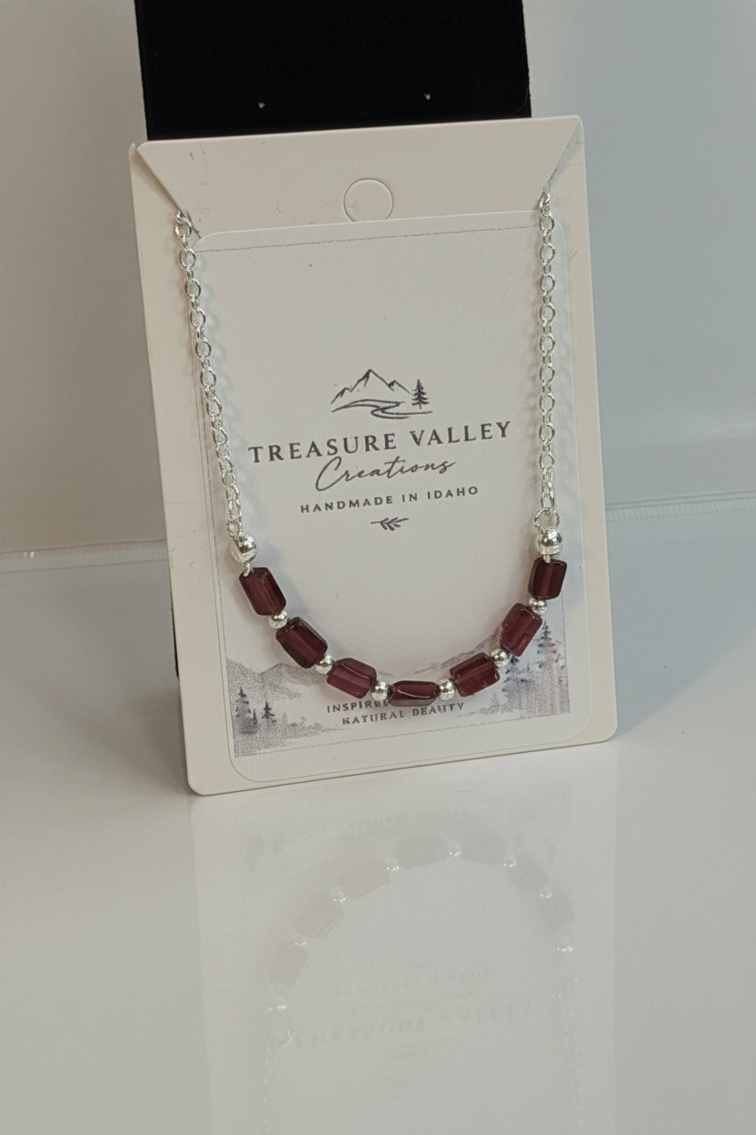 Treasure Valley Creations bracelet with dark red faceted beads and silver chain, displayed on its branded white backing card.