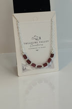 Treasure Valley Creations bracelet with dark red faceted beads and silver chain, displayed on its branded white backing card.