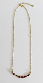 A gold chain necklace with a small cluster of dark red beads at the bottom, displayed on a plain light gray surface.