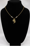 A gold chain necklace with a rose-shaped pendant and three small pearl-like beads, displayed on a black jewelry bust against a light gray background.