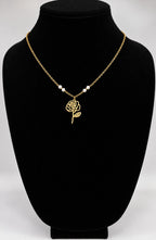 A gold chain necklace with a rose-shaped pendant and three small pearl-like beads, displayed on a black jewelry bust against a light gray background.