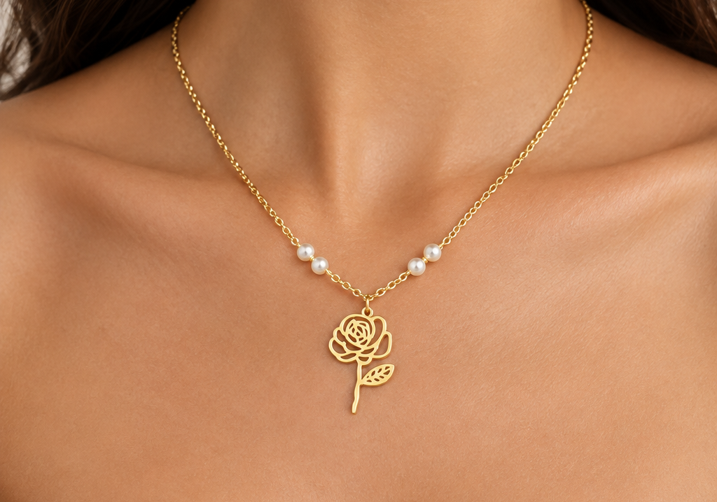 A close-up of a model's neck and chest wearing a delicate gold chain necklace with a rose pendant and small white pearl accents.