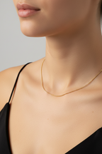Gold necklace worn by a model against a neutral background