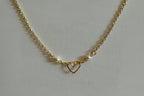 A gold chain necklace featuring a central open heart pendant and two small white pearl beads on either side, displayed on a textured light gray fabric background.