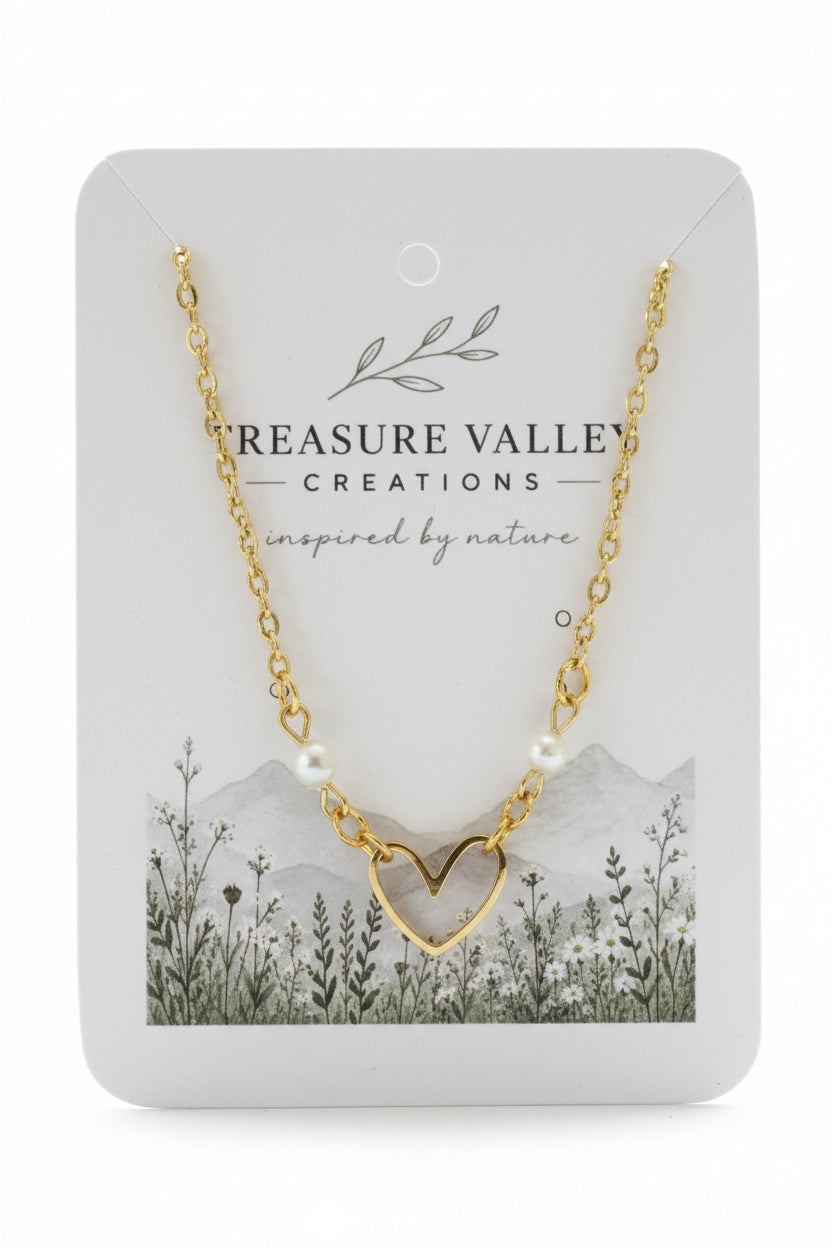 A gold chain necklace with a heart-shaped pendant and small pearl beads, displayed on a white card from Treasure Valley Creations.