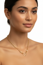 A close-up of a woman wearing a delicate gold chain necklace with a small open heart pendant and two pearl-like beads, shown against a clean white background.