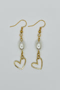 A pair of gold dangle earrings featuring a freshwater pearl and an open heart-shaped gold pendant, displayed on a neutral light gray background.