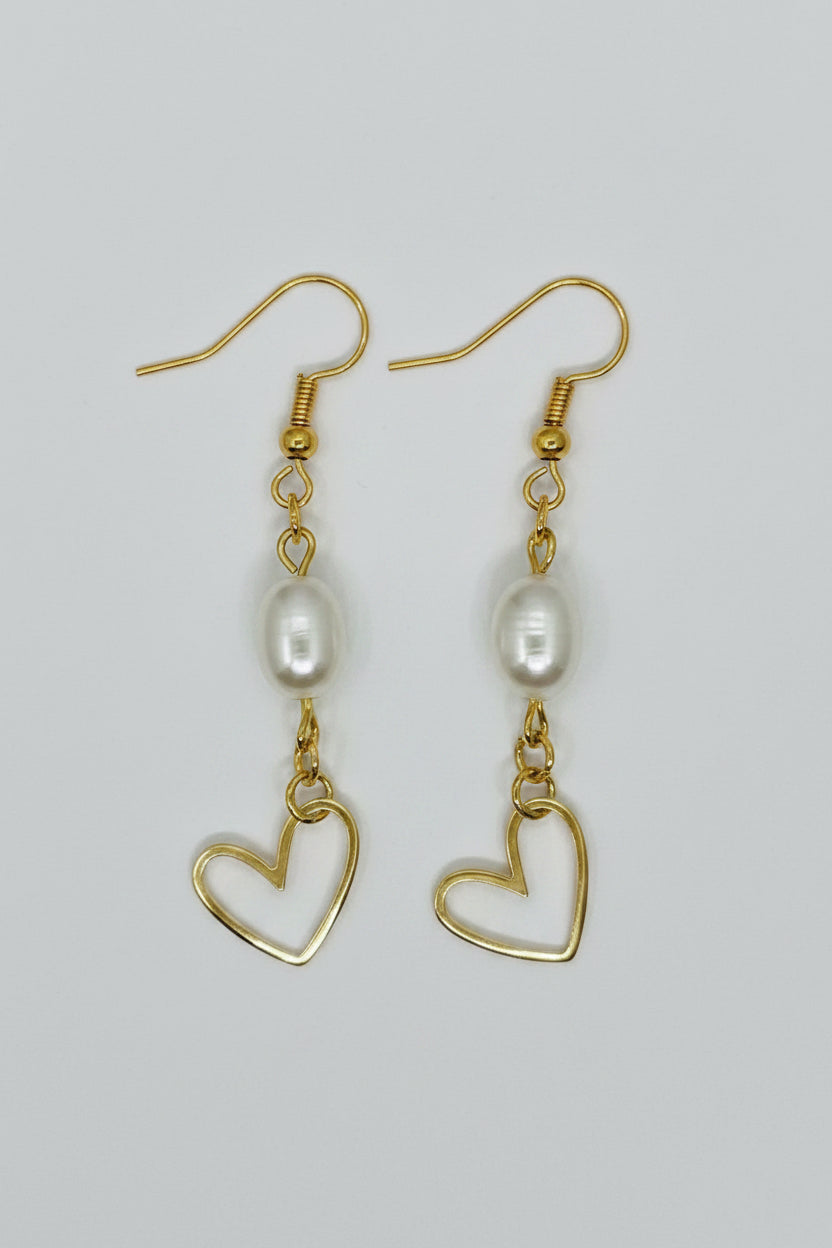 A pair of gold dangle earrings featuring a freshwater pearl and an open heart-shaped gold pendant, displayed on a neutral light gray background.