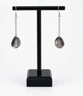 A pair of silver drop earrings with faceted teardrop-shaped smoky gray crystal pendants, displayed on a black T-stand against a white background.