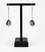A pair of silver drop earrings with faceted teardrop-shaped smoky gray crystal pendants, displayed on a black T-stand against a white background.