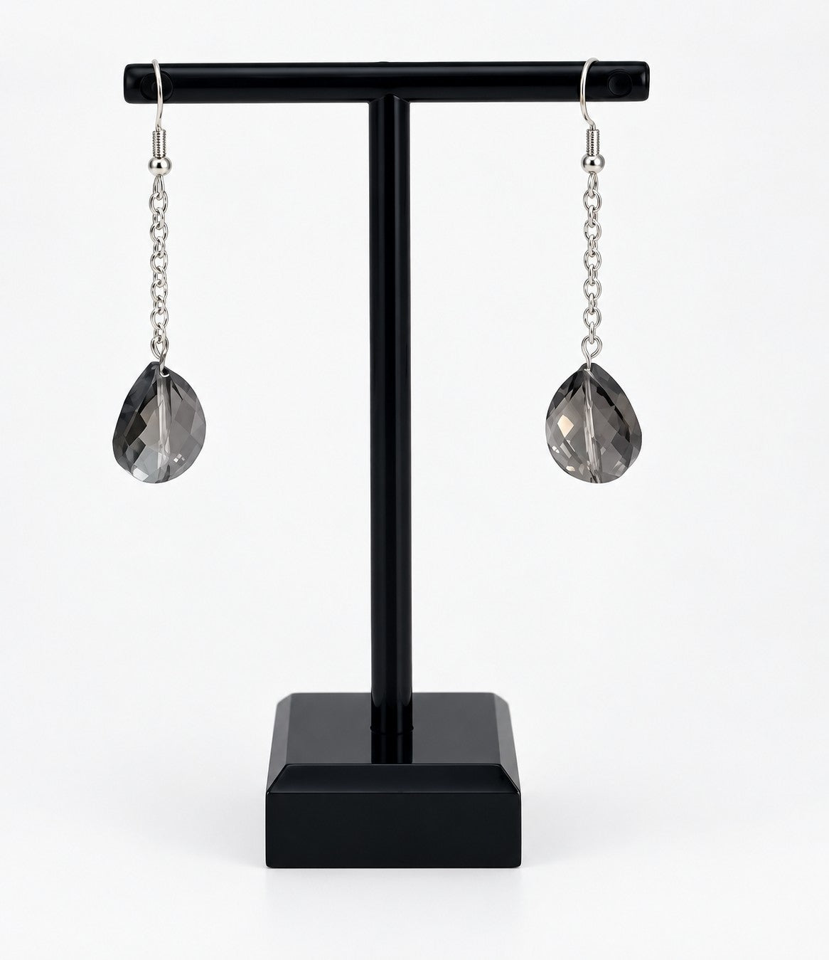 A pair of silver drop earrings with faceted teardrop-shaped smoky gray crystal pendants, displayed on a black T-stand against a white background.