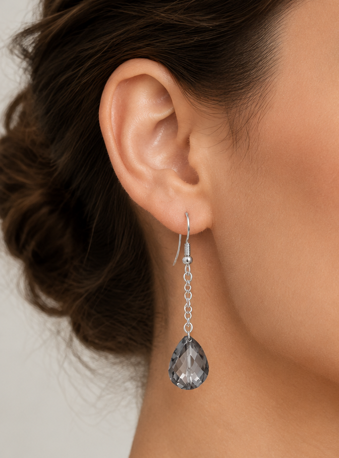 A close-up of a model's ear wearing a silver drop earring with a faceted gray teardrop crystal pendant.